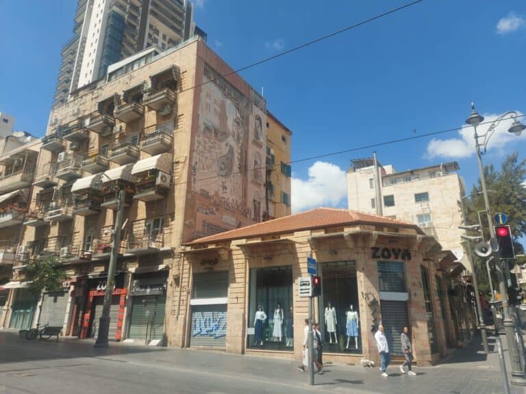ציור הקיר האייקוני ברחוב יפו, סמוך לשוק מחנה יהודה בירושלים, תחת שמיים כחולים, על רקע חנויות סגורות