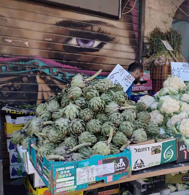 דוכן ארטישוקים טריים בשוק מחנה יהודה, ברקע ציור רחוב צבעוני