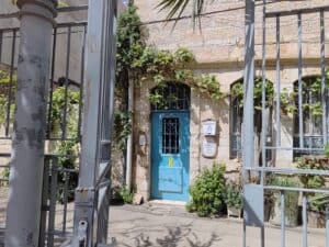 : שער הכניסה לבית אבן עם דלת כחולה ופס צהוב - סימן תמיכה בחטופים