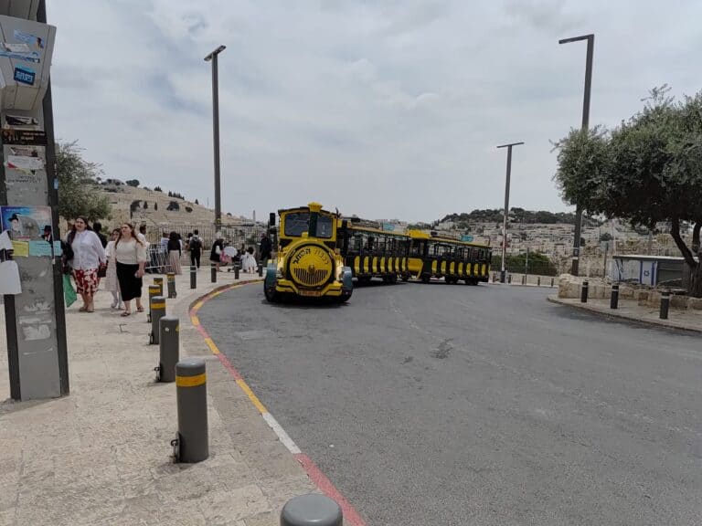 A yellow tourist tram passes through the Old City of Jerusalem, alongside a group of ultra-Orthodox women