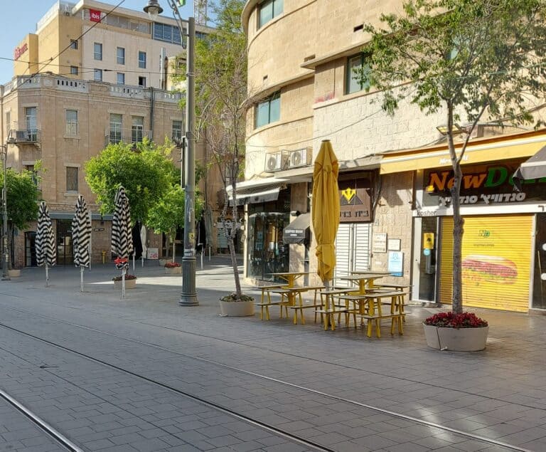 רחוב שקט בירושלים בערב שבת, עם חנויות סגורות ועצים. משקף אווירה אופיינית לשבת בחלקים מסוימים של העיר.