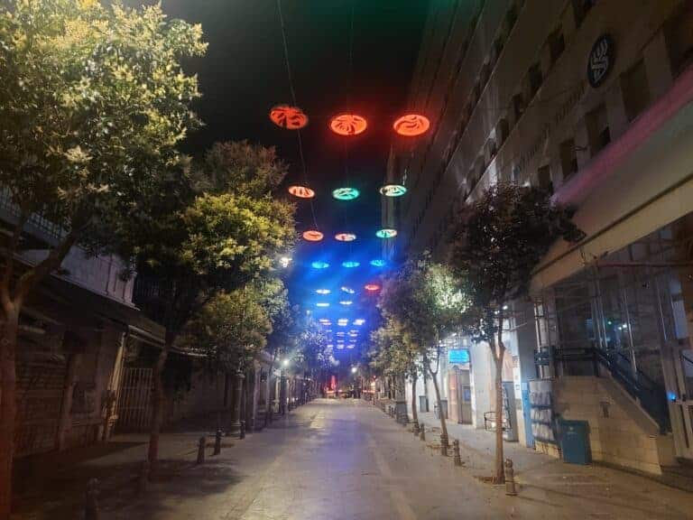 Jerusalem’s city center at night during wartime: colorful lights, empty road, and looming tension