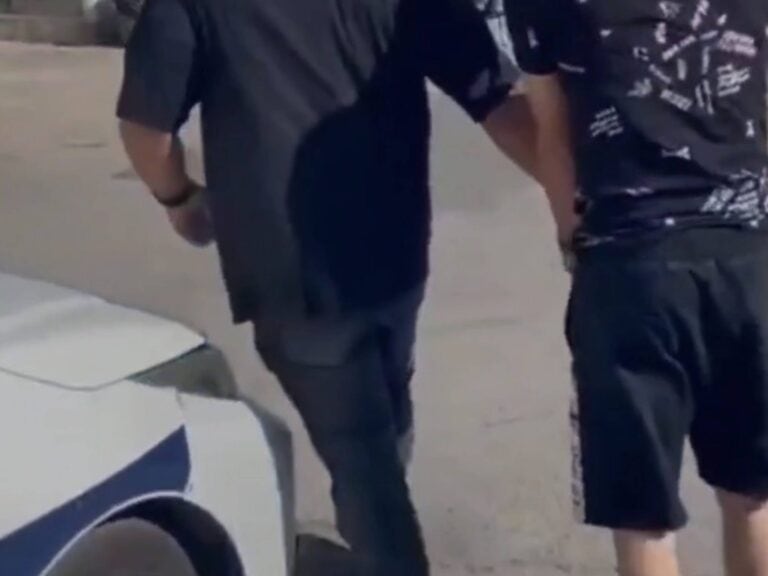 A suspect is escorted by officers near a police vehicle in Jerusalem, following arrest over pro-Iran social media content