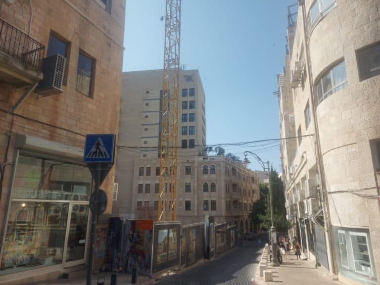 Jerusalem street near Waldorf Astoria with crane, stone buildings, and pedestrians in summer light