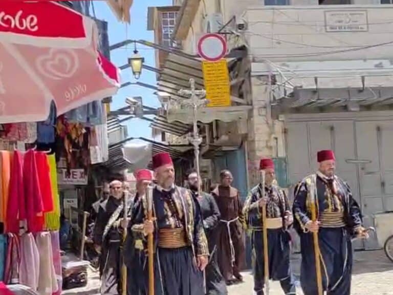 Christian monks in black robes march through Jaffa Gate market in Jerusalem, carrying ritual wooden staffs
