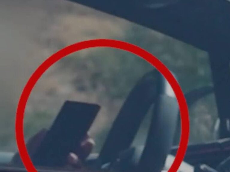 A driver caught using a mobile phone while driving near Jerusalem, captured through the windshield
