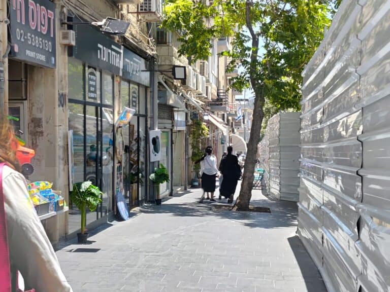Sunny sidewalk in central Jerusalem with people walking under partial shade