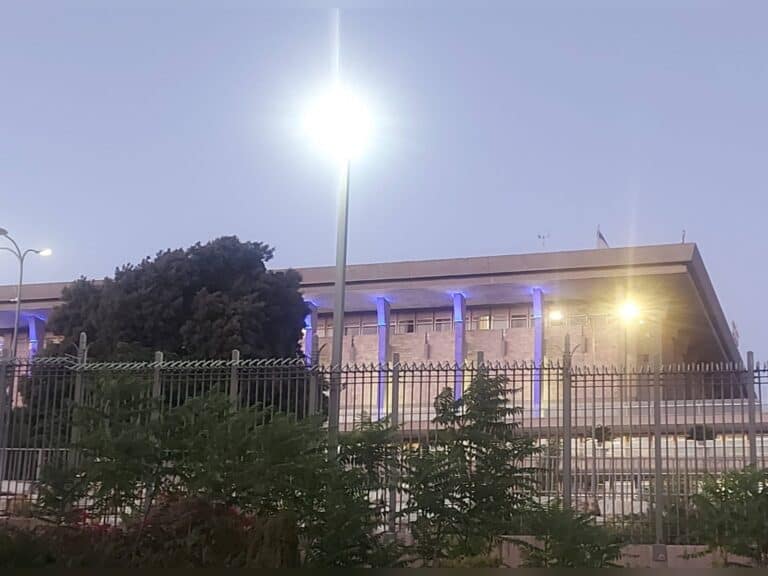 Night view of the Israeli parliament glowing in symbolic blue light, reflecting disconnect between state and society in Jerusalem