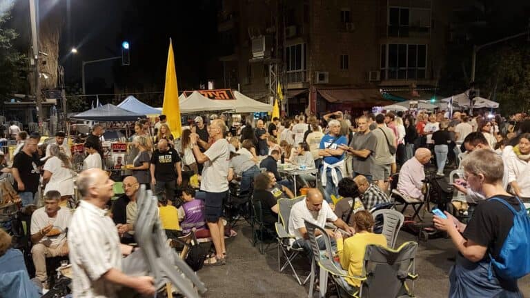 Families and supporters in a protest tent on Gaza Street in Jerusalem during Rosh Hashanah, sharing a somber holiday meal on the road