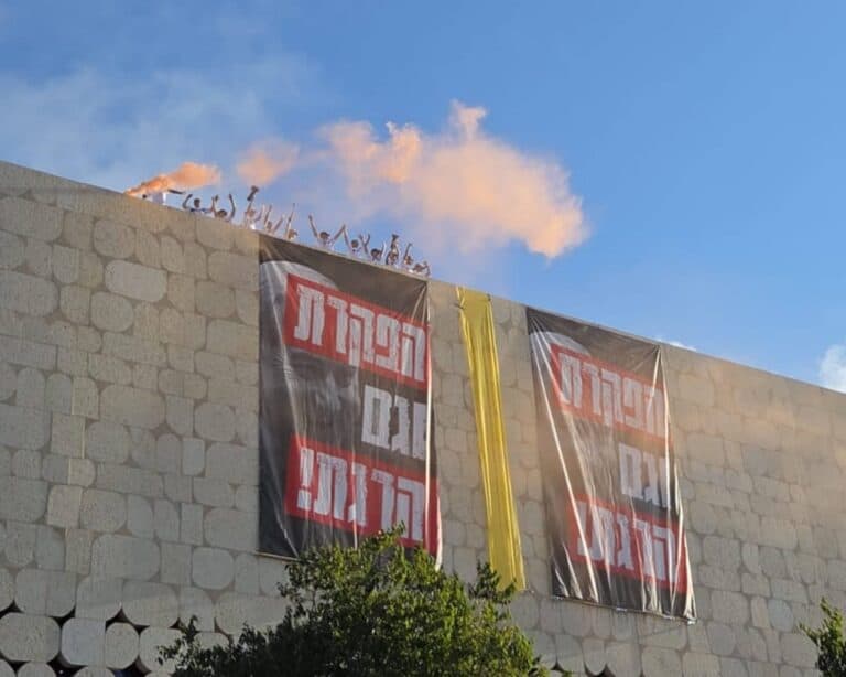 מפגינים על גג עם רימון עשן ושלטים בגבעת רם במחאת החטופים בירושלים