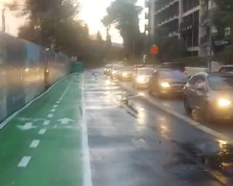 שביל אופניים רטוב מגשם ומדרכה רחבה להולכי רגל בציר דרך בית לחם בירושלים לצד טור רכבים עומדים בגשם