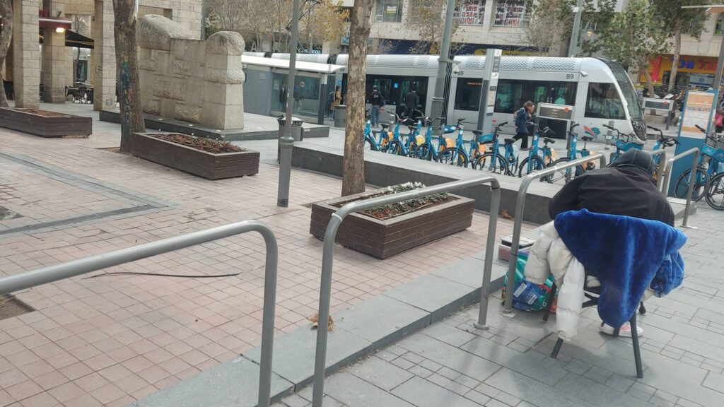 דר רחוב יושב על כיסא מאולתר בכיכר הדוידקה במרכז העיר ירושלים לאחר הסרת הספסלים