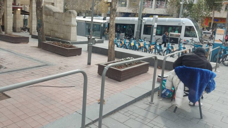 דר רחוב יושב על כיסא מאולתר בכיכר הדוידקה במרכז העיר ירושלים לאחר הסרת הספסלים