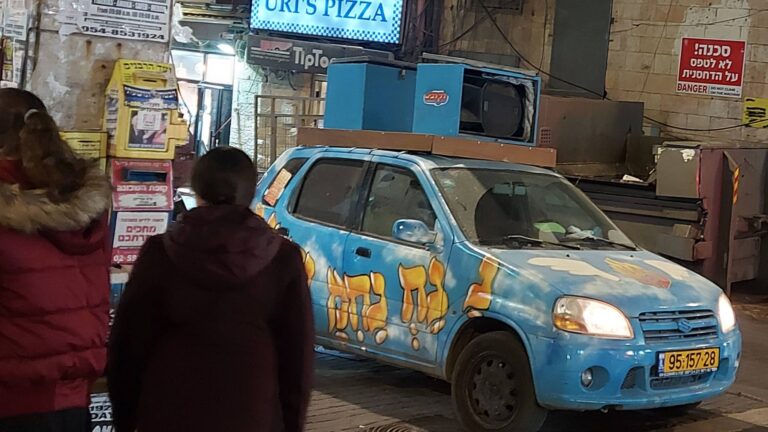 רכב עם ציור בעברית ברחוב בשכונה חרדית בירושלים סמוך לחנויות תחפושות לקראת פורים