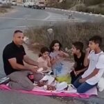 A father from Beit Iksa eats with his children near the military checkpoint after being barred from entering the village