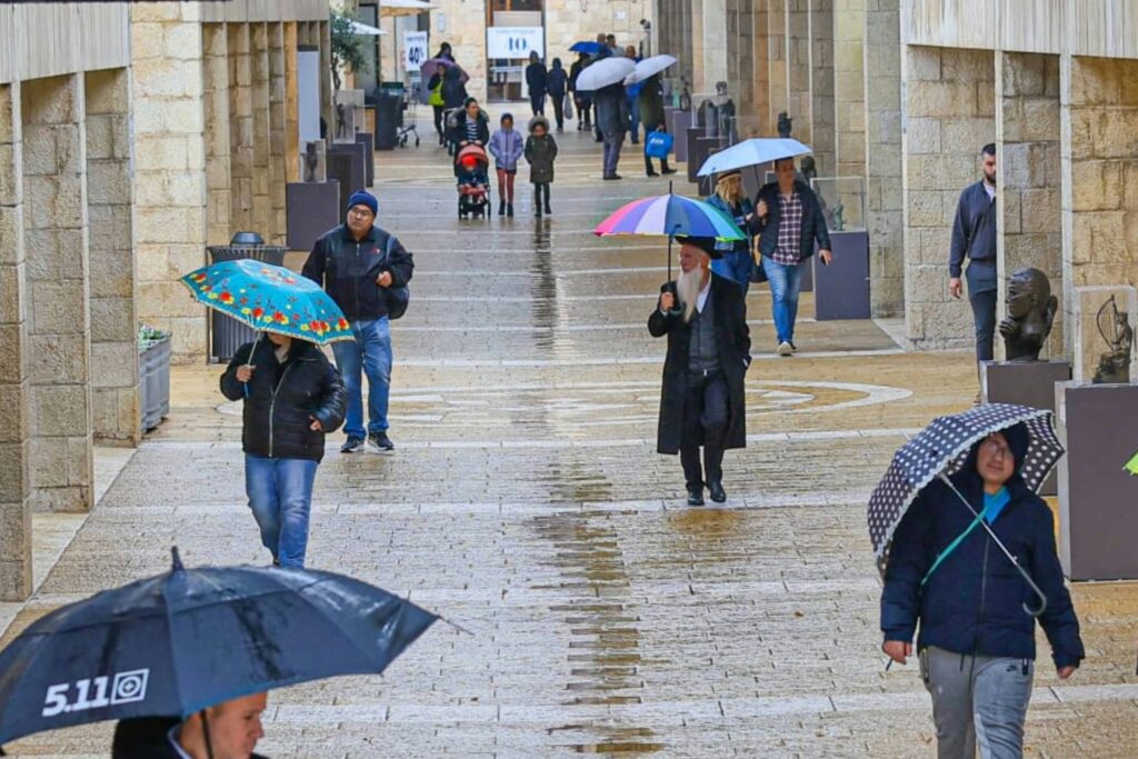 תושבים הולכים עם מטריות בגשם ברחובות ירושלים לקראת חורף תשפ"ז 2026-2027